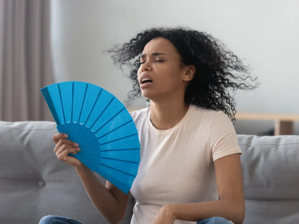 A young woman fanning herself, looking uncomfortable in a hot room.